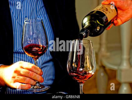 Versando un bicchiere di vino rosso in mano e il vino rosso in un bicchiere Foto Stock