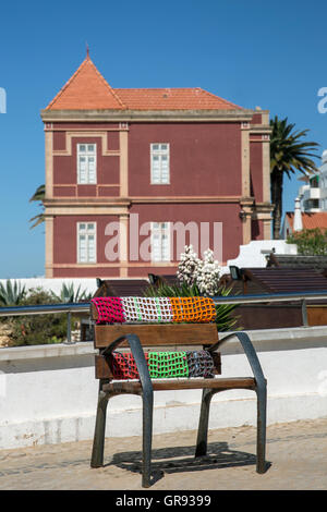 Cadeira Com Enfeite De Lã Na Frente de Uma casa Marrom-Avermelhada Em Armação de Pêra, Algarve, Portogallo, Europa Foto Stock