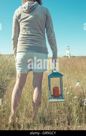 Una donna in possesso di una lanterna con un faro in distanza, di New London, Prince Edward Island, Canada. Foto Stock