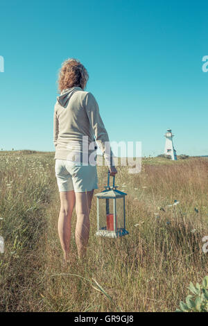 Una donna in possesso di una lanterna con un faro in distanza, di New London, Prince Edward Island, Canada. Foto Stock