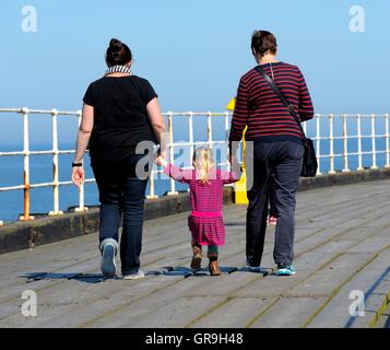 La nonna e la madre tenendo le mani con un bimbo piccolo ragazza sul molo di Whitby North Yorkshire England Regno Unito Foto Stock
