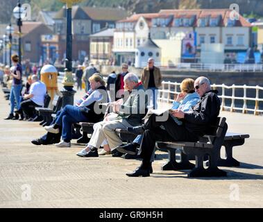 Vacanzieri seduti sui banchi a Whitby Yorkshire England Regno Unito Foto Stock