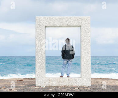 Giovane uomo in piedi in un calcestruzzo cuboide e guarda al mare Foto Stock