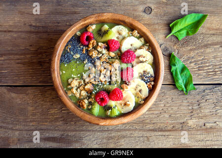 Una sana colazione frullato verde ciotola guarnita con frutta, bacche e i semi di più rustico sfondo di legno Foto Stock