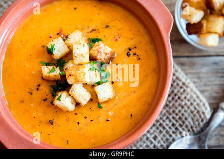 Verdure zuppa di pomodoro e carote con crostini e prezzemolo in vaso di ceramica oltre rustico sfondo di legno vicino fino Foto Stock