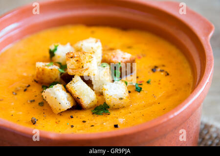 Verdure zuppa di pomodoro e carote con crostini e prezzemolo in vaso di ceramica oltre rustico sfondo di legno vicino fino Foto Stock