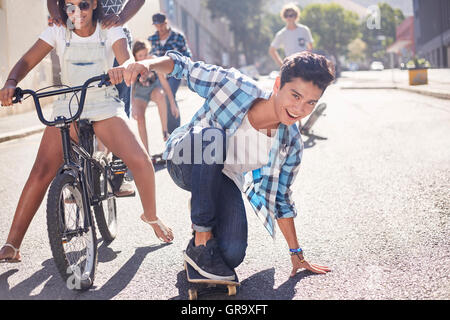Ritratto sorridente ragazzo adolescente lo skateboard con gli amici di sunny strada urbana Foto Stock
