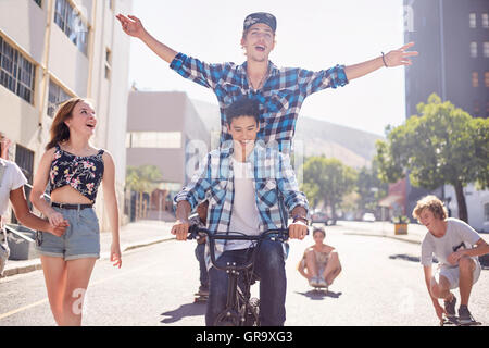 Amici di adolescenti di equitazione biciclette BMX e skateboard su soleggiate strada urbana Foto Stock