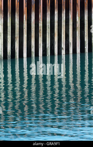 Un acciaio arrugginiti seawall si riflette in leggermente increspata blu verde acqua. Foto Stock