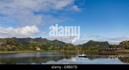 Il Vestfjorden Kabelvag in blu con la barca da pesca e Rorbu-Huts, Lofoten, Isola Ausvagoy, Norvegia Foto Stock