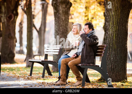 Coppia senior seduta sul banco, bere caffè. La natura in autunno. Foto Stock