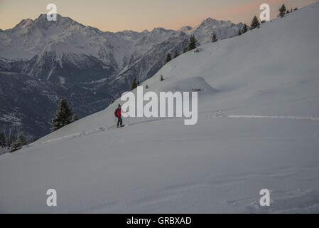 Femmina Snowshoer all'alba, si muove in salita su un Snowfield, sullo sfondo delle montagne innevate Foto Stock