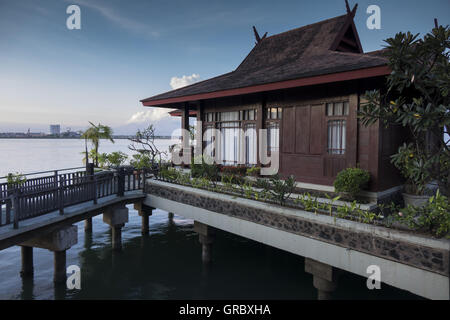 In primo piano molo che conduce a uno stile tradizionale Palafitta, In Backgrond mare, cielo blu e la costa con edifici industriali. Makassar, Sulawesi meridionale, Indonesia Foto Stock