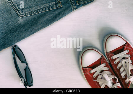 Coppia di red sneakers, frammento retrò jeans, occhiali da sole nero su bianco sullo sfondo di legno, vintage styling Foto Stock