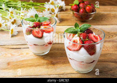 Le fragole layered il formaggio cremoso dessert su sfondo di legno. Panna montata con fragole fresche. Foto Stock