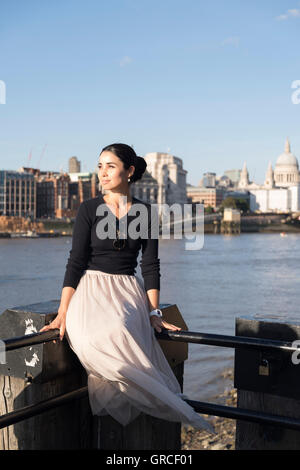 Donna seduta accanto al Fiume Tamigi con la Cattedrale di San Paolo in background. Londra, Inghilterra Foto Stock