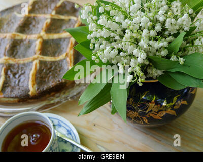 Teatime, semi di papavero torta, insieme con il giglio della valle bouquet e una tazza di tè Foto Stock