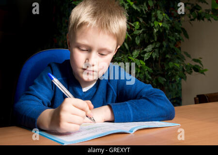 Giovane ragazzo caucasico facendo la sua scuola elementare dovere mentre seduto alla scrivania. Foto Stock