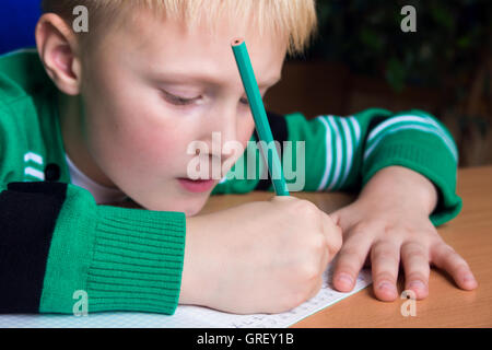 Giovane ragazzo caucasico facendo la sua scuola elementare dovere mentre seduto alla scrivania. Foto Stock