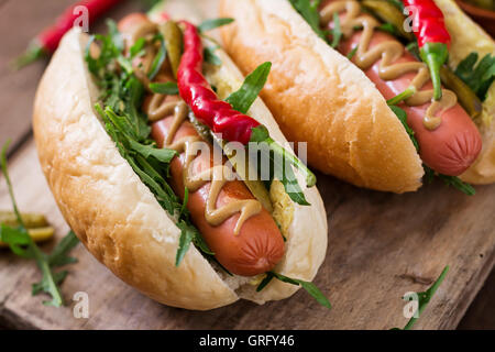 Hot Dog con sottaceti, capperi e rucola su sfondo di legno. Foto Stock