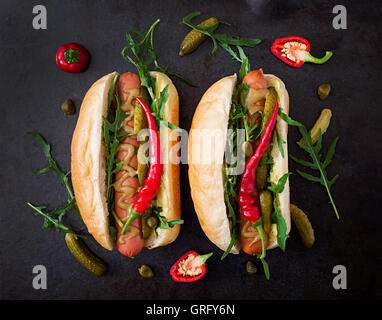 Hot Dog con sottaceti, capperi e rucola su sfondo di legno. Foto Stock