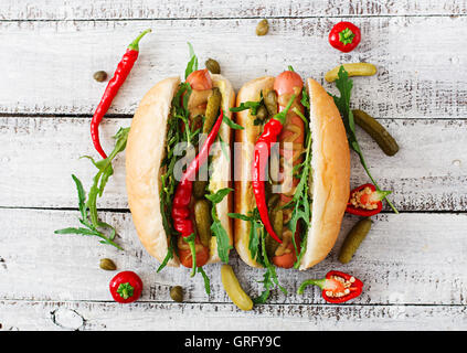 Hot Dog con sottaceti, capperi e rucola su sfondo di legno. Vista superiore Foto Stock