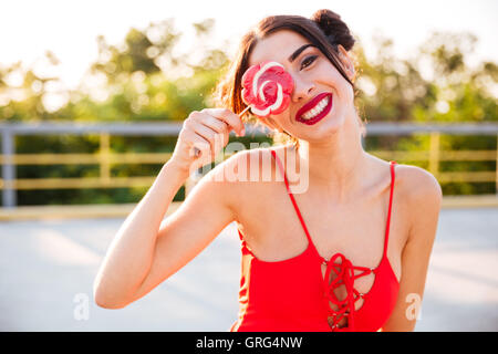 Allegro giocoso giovane donna coperto il suo occhio con lollipop in piedi all'aperto Foto Stock