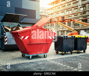 Dumpster rosso, il riciclaggio dei rifiuti e cassonetti vicino al nuovo edificio per uffici. Sito in costruzione sullo sfondo Foto Stock