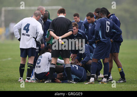 La preoccupazione per un giocatore ferito durante un Hackney & Leyton League match tra Eureka FC (blu) e Mile End FC a Hackney paludi Foto Stock