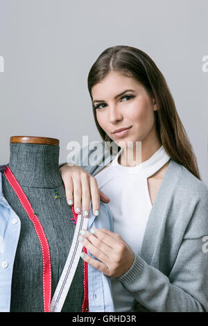 Una giovane donna bellissima funziona su un manichino sarti come una sarta Foto Stock