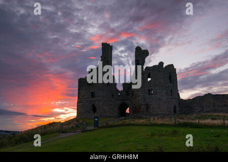 Il presagio rovine del castello di Dunstanburgh al tramonto sulla costa del Northumberland, England Regno Unito Foto Stock