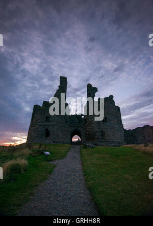 Il presagio rovine del castello di Dunstanburgh al tramonto sulla costa del Northumberland, England Regno Unito Foto Stock