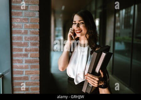 Imprenditrice che trasportano le cartelle e parlando al telefono Foto Stock