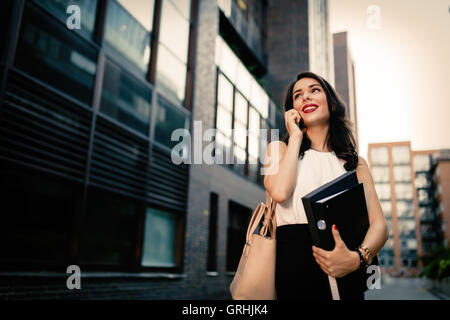 Imprenditrice che trasportano le cartelle e parlando al telefono Foto Stock