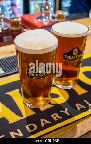 Due pinte di real ale in Theakston occhiali di marca su una barra Theakston asciugamano, due volte prodotta Inn, una volta prodotta, Cumbria, Inghilterra Foto Stock