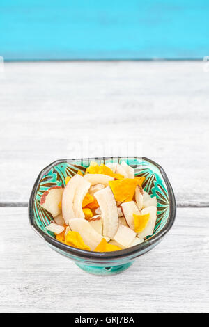 Noce di cocco essiccata e fette di mango in una ciotola verde sul tavolo rustico, spazio per il testo. Foto Stock