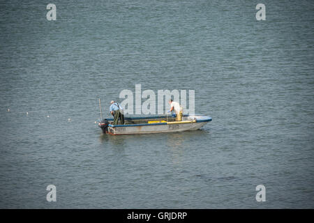 Due pescatori per la cattura di pesce con reti da una piccola barca nel porto di Portsmouth Foto Stock