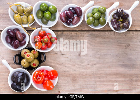 Confine assortiti di nero, verde e olive ripiene e il verde e il rosso pimento peperoni in bianco piccoli piatti in ceramica su un di legno Foto Stock