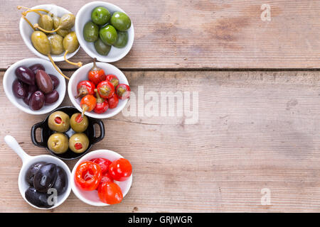 Assortimento di nero indurito, verde e farcito di olive salate e colorate di rosso pimento peperoni in piccole ciotole raggruppati su una Foto Stock