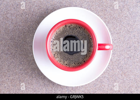 Bicchiere di fresco energizzante caffè nero versata in un bicchiere di rosso su un piattino bianco centrato su un tessuto grigio sfondo Foto Stock