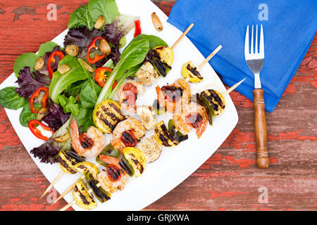 Tre gourmet spiedini di gamberi o spiedini con insalata verde, pomodori e peperoni dolci a basso angolo vicino a un tavolo per la cena. Servita w Foto Stock