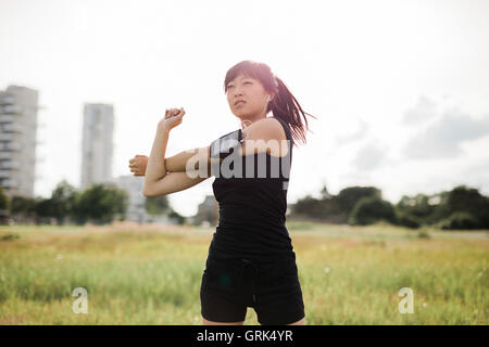 Colpo di montare la giovane donna stiro a parco urbano. Cinese modello femminile in sportswear facendo esercizio di riscaldamento in un parco in mattinata Foto Stock