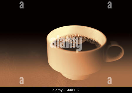 Tazza di caffè su un tavolo di vetro in seppia. White Tazza da caffè Close Up con sfondo scuro e luce drammatica. Foto Stock