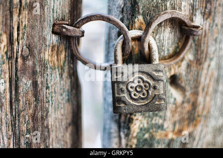 Vecchio arrugginito lucchetto decorato su una porta di legno. Vintage lucchetto corrosi su un antico cancello dello sfondo. Foto Stock