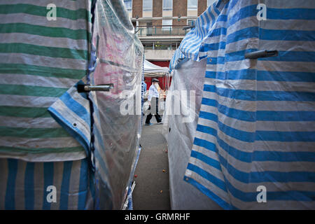 Uomo che cammina attraverso il mercato di strada visto tra i teloni di Market Stall Foto Stock