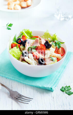 Tonno e insalata di pasta con pomodori freschi, olive, erbe aromatiche in vaso bianco su sfondo di legno Foto Stock