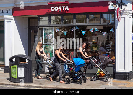 Tre giovani madri passano dalla Costa cafe su Westow Street in Crystal Palace di Londra England Regno Unito Regno Unito Foto Stock