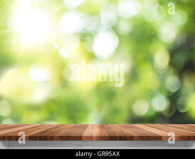 Vuoto in legno marrone del tavolo con Sun e la sfocatura di green tree sfondo bokeh, modello mock up per il montaggio del prodotto. Foto Stock