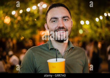 Bello barbuto uomo europeo bevendo cocktail o una birra presso outdoor Street Cafe festa notturna nel parco Foto Stock