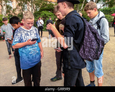 Copenhagen, Danimarca, Large Group Young People, Danish Children Playing Smart Phone Game 'Pokemon Go' in Public Park, Holding iPhone (Danish Jewish Mu-seum Garden) Group teenagers talking, looking phones, students in Park, smartphone dependency teens on their phone Foto Stock